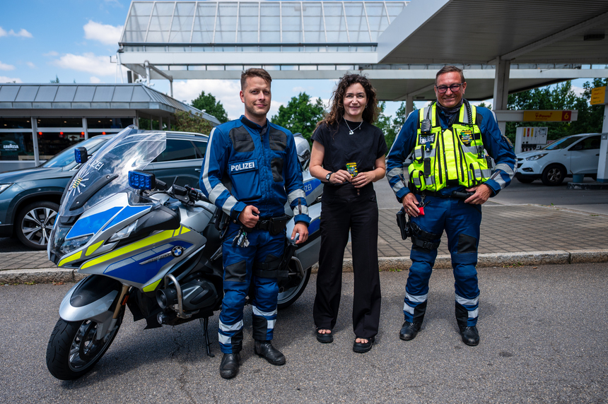 Justizministerin Constanze Geiert steht zwischen zwei Polizisten der Motorradstaffel neben einem Polizeimotorrad