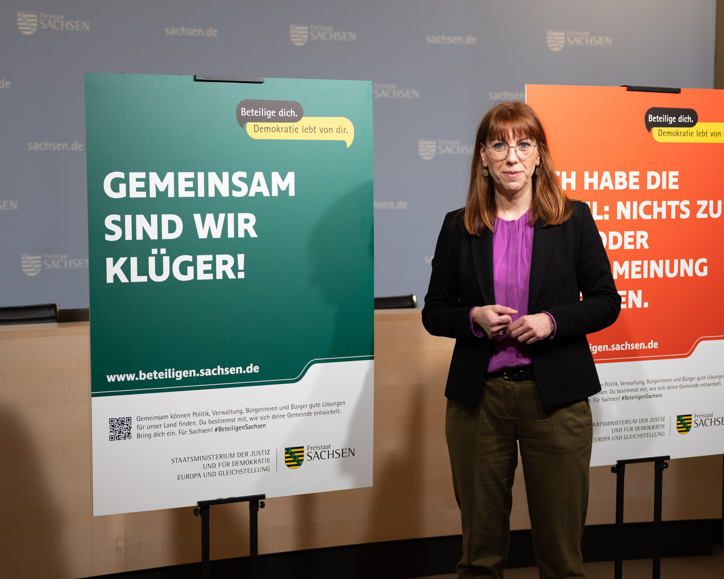 Demokratieministerin Katja Meier steht neben einem Plakat mit der Aufschrift: Gemeinsam sind wir klüger.