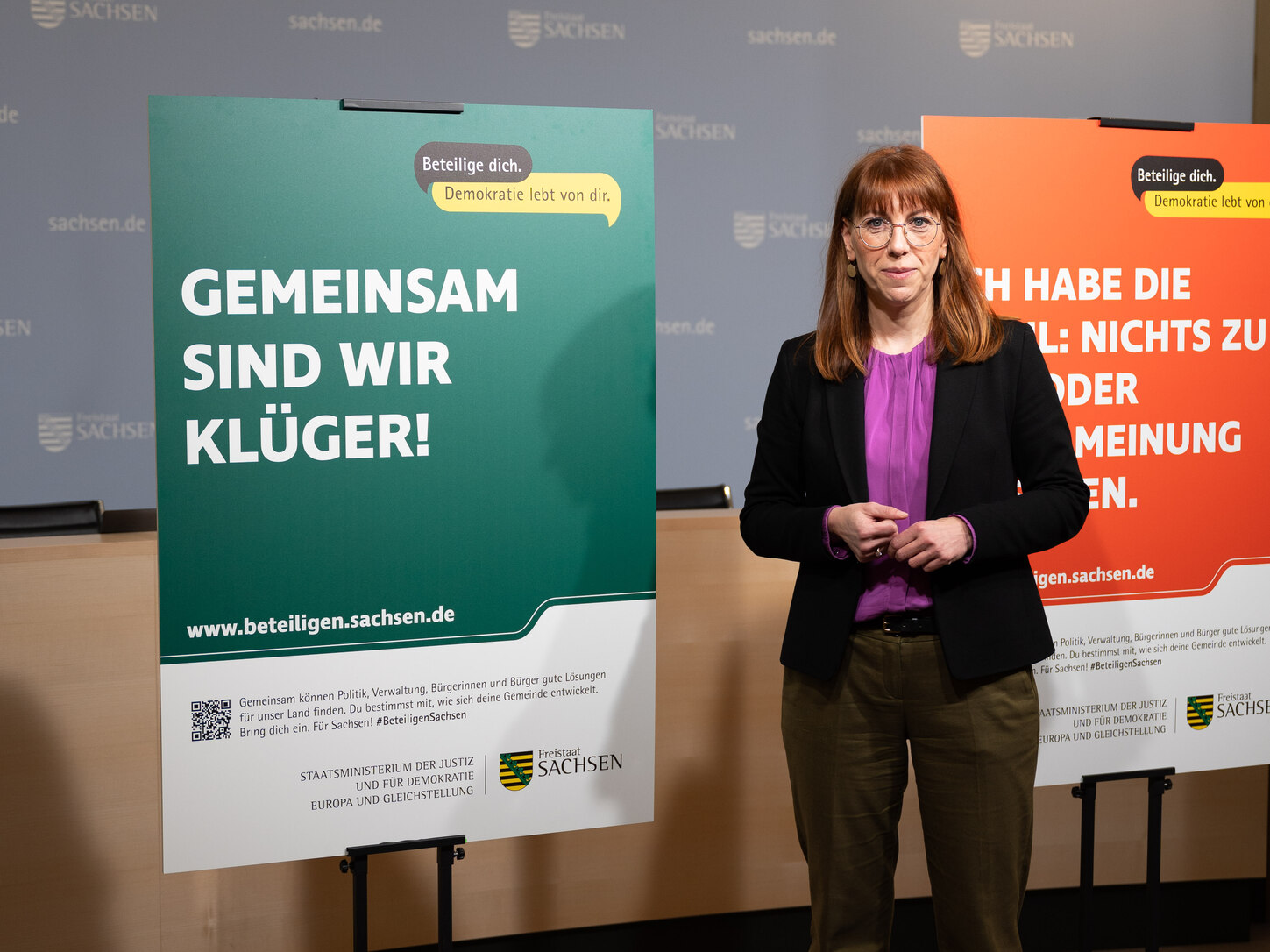 Demokratieministerin Katja Meier steht neben einem Plakat mit der Aufschrift: Gemeinsam sind wir klüger.