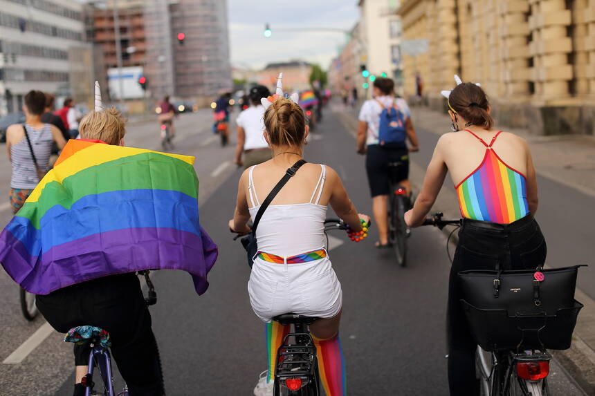 viele Menschen auf Fahrrädern, einer hat eine Regenbogenflagge auf seinem Rücken