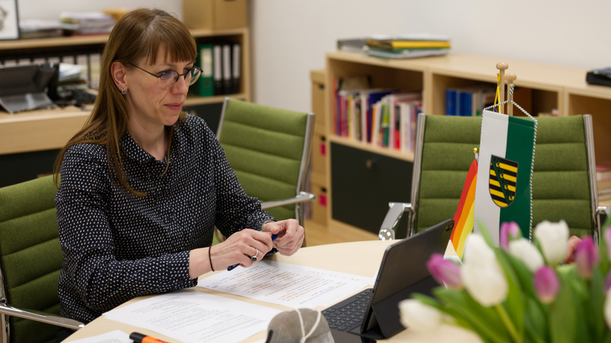 Kajta Meier Mit Laptop, Stift, Papier, FFP2-Masket und einem Strauß tulpen auf dem Tisch bei einer Videokonferenz mit Studenten aus Breslau